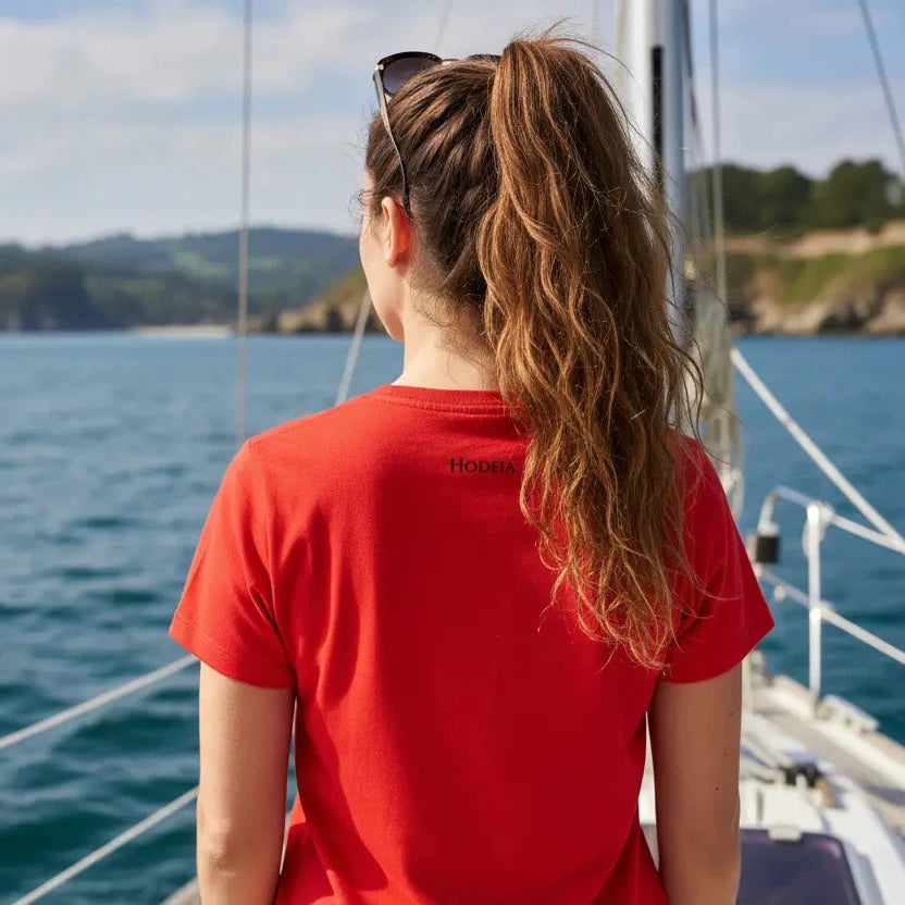 femme portant le t-shirt coton cintré femme insola coloris rouge logo noir de dos sur un bateau de plaisance