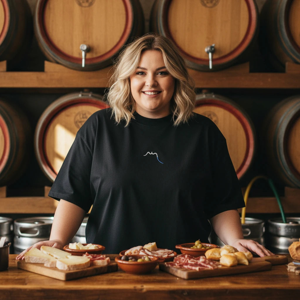 femme portant le t-shirt grande taille en coton bio brodé le pottolo coloris noir devant un bar à tapas dans une cidrerie au pays basque