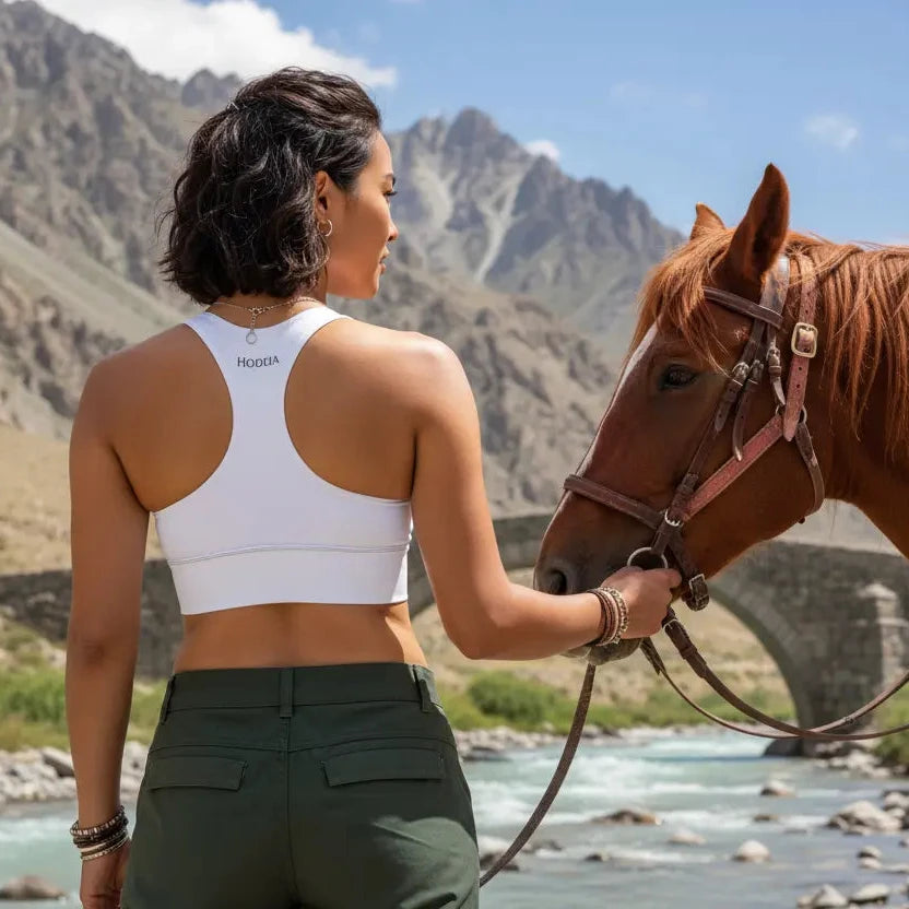 femme portant la brassière de sport éco-responsable carlina coloris blanc tenant un cheval par la bride à la montagne