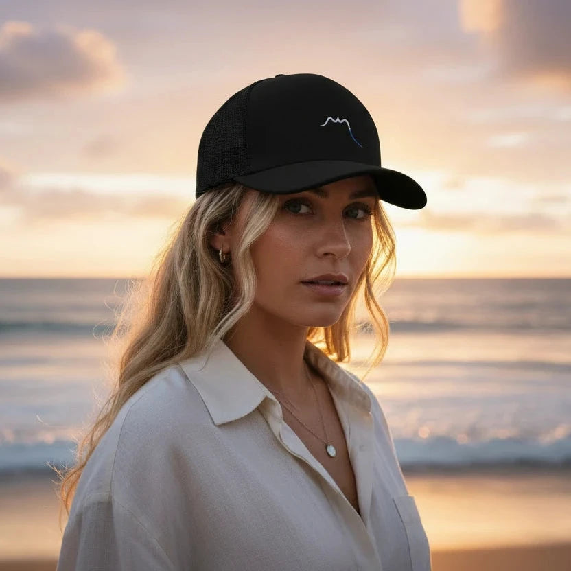 femme portant la casquette de camionneur respirante légère et réglable coloris noir avec logo blanc à la plage