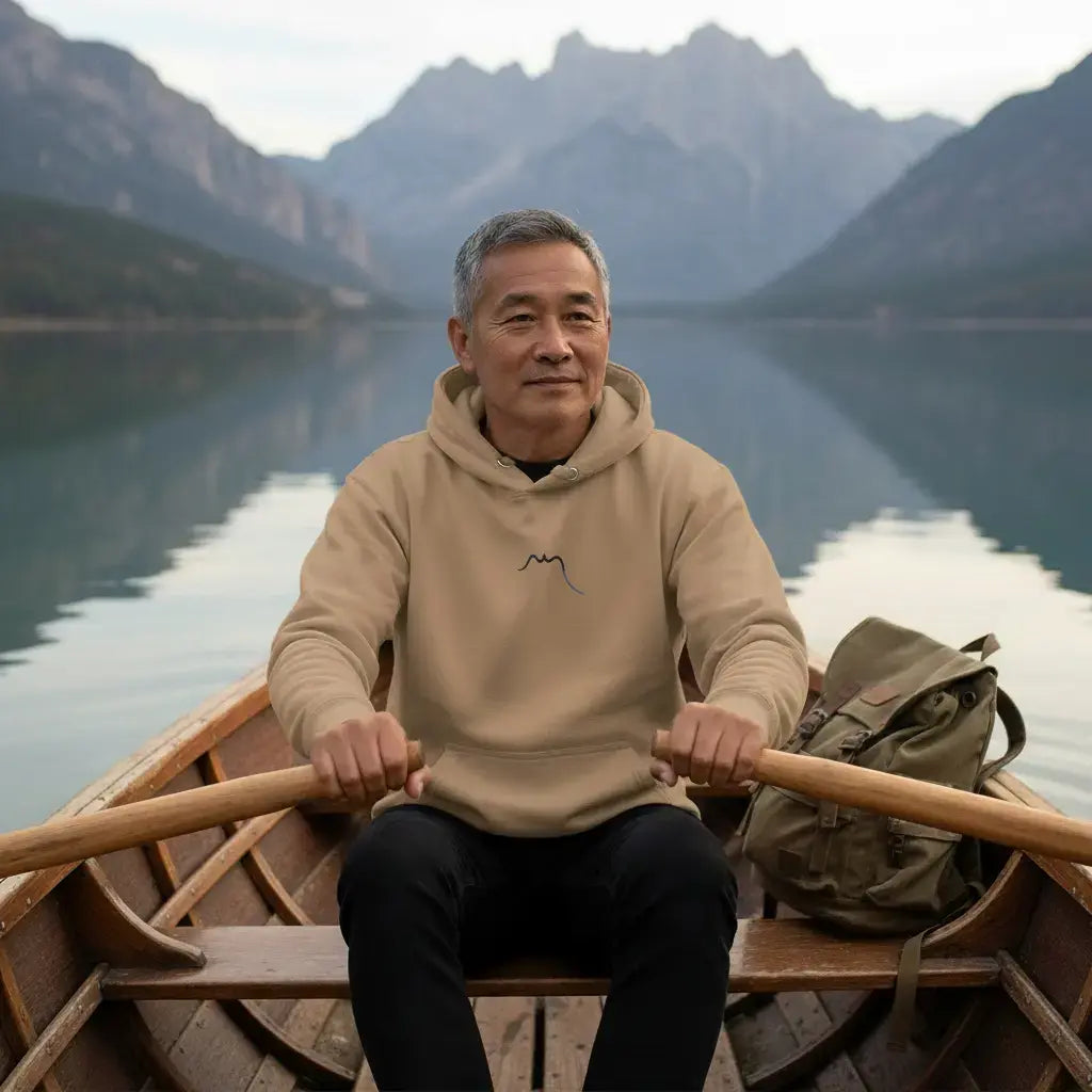 homme portant le hoodie en coton bio negua coloris brun ramant dans une barque sur un lac de montagne