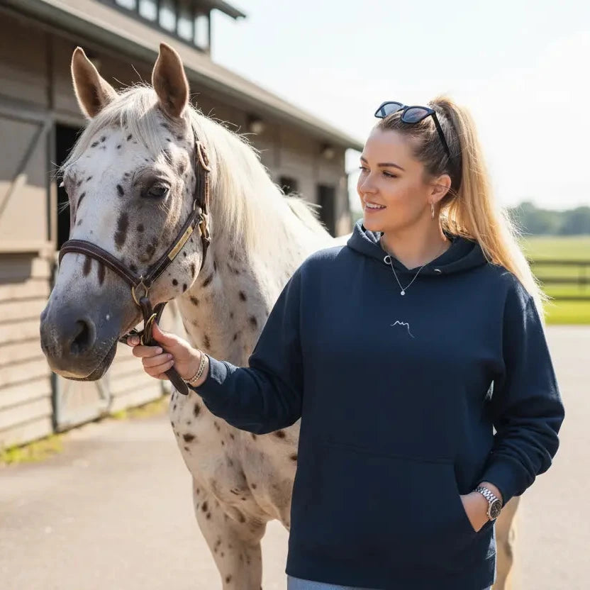 femme portant le hoodie en coton bio negua coloris bleu marine avec un cheval devant des écuries