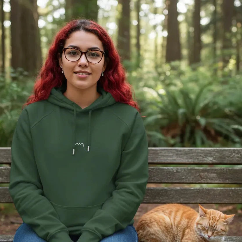 femme portant le hoodie sweat à capuche femme homme en coton biologique hotza coloris vert forêt assise sur un banc avec un chat en pleine nature