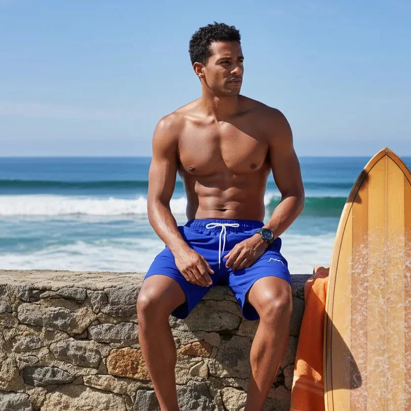 homme portant le maillot de surf indar coloris bleu roi devant un spot de surf