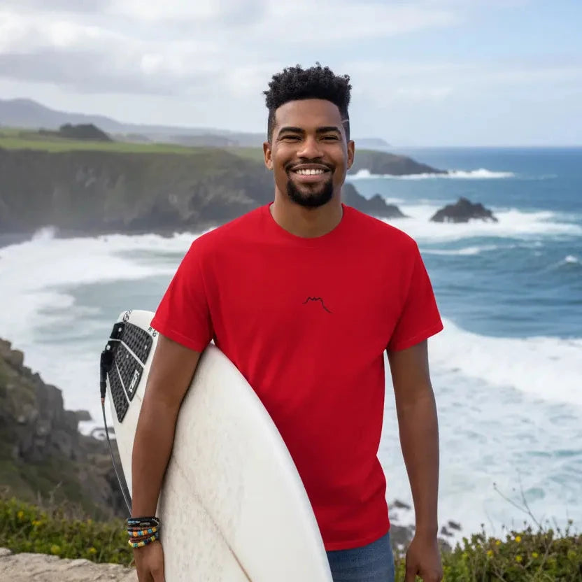 homme portant le t-shirt coton femme homme l'ermite coloris rouge avec une planche de surf devant l'océan